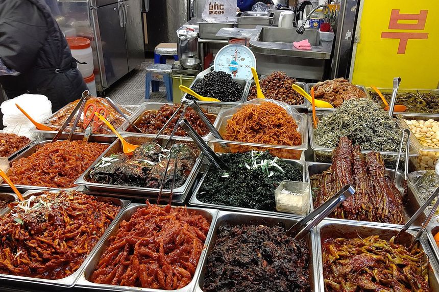 Trays of prepared Korean side dishes heaped along a stall counter at Gwangjang Market.