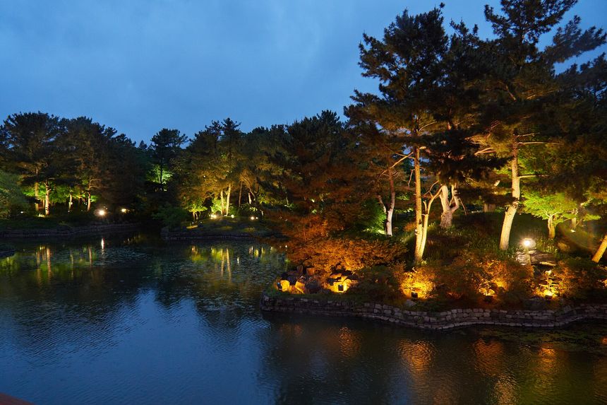 The illuminated pavilions of Donggung Palace mirrored in the still water of Wolji Pond at blue hour.